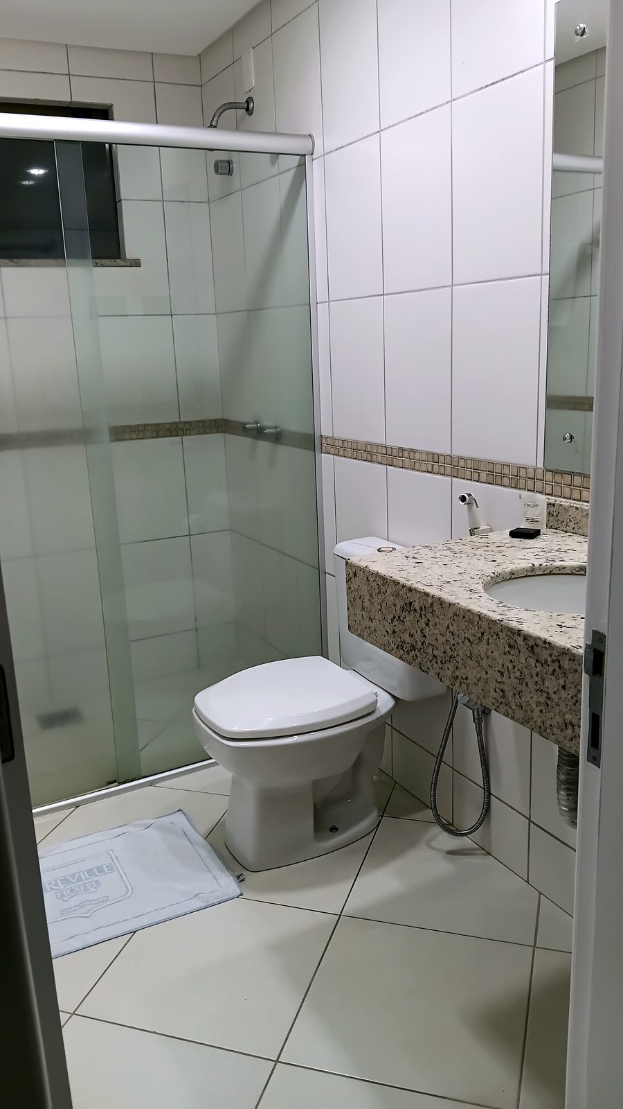 Banheiro do apartamento Luxo do Treville Hotel com bancada em granito e box de vidro